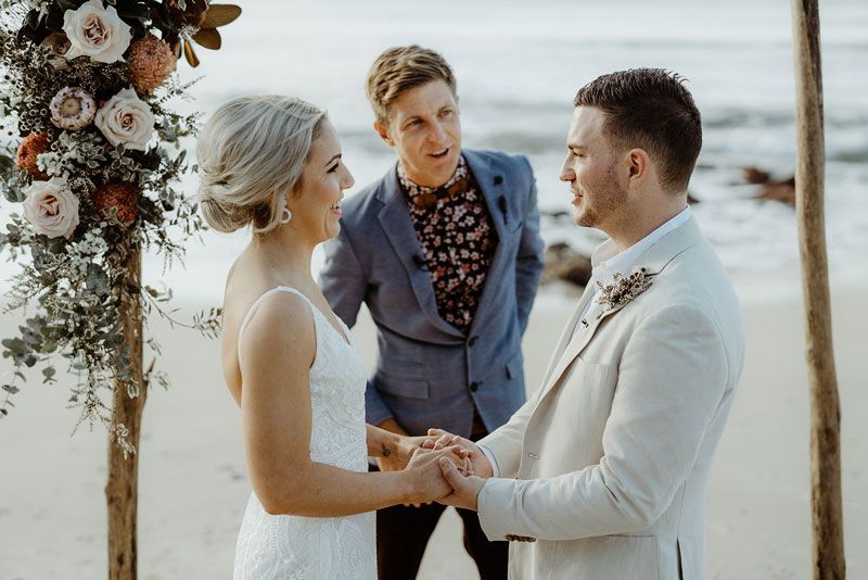 A bride and groom are holding hands during their wedding ceremony on the beach.