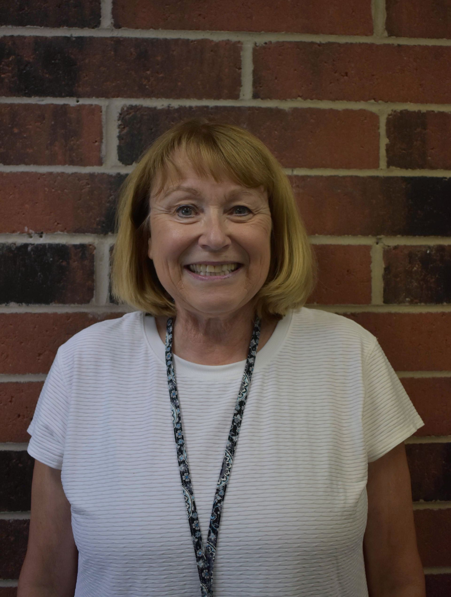 A woman wearing a brookridge day school shirt is smiling in front of a brick wall.