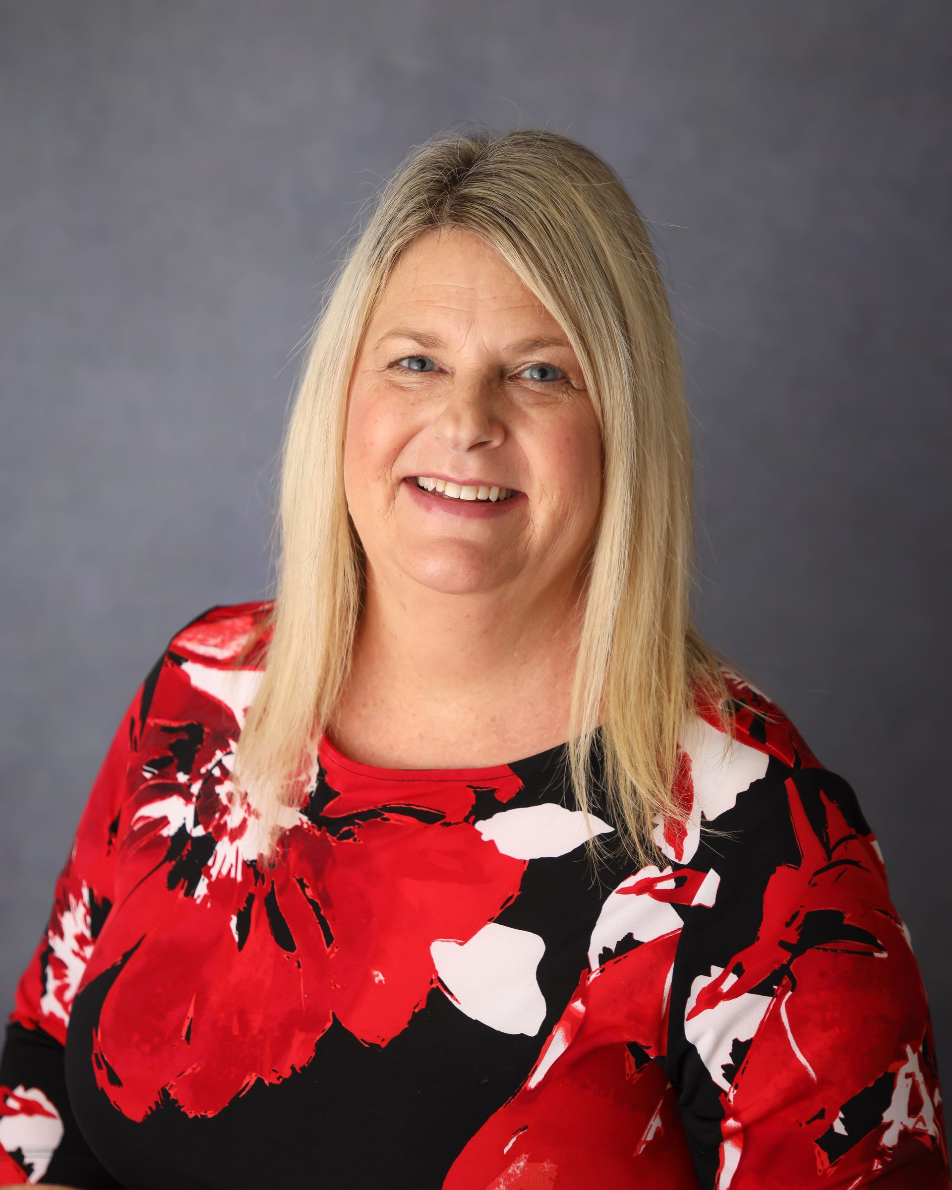 A woman in a red and black floral dress is smiling for the camera.