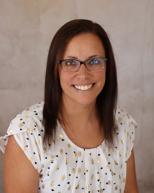 A woman wearing glasses and a pink shirt is smiling for the camera.