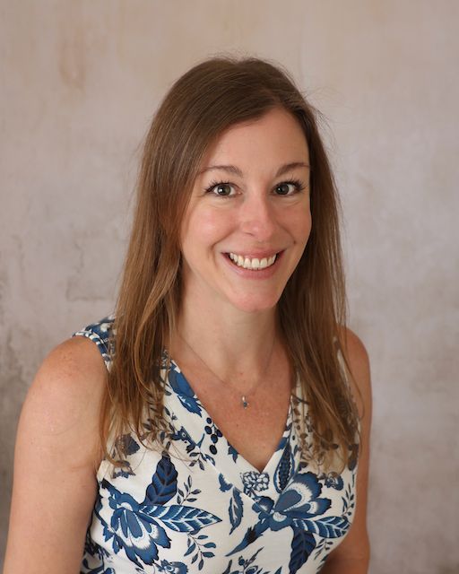 A woman wearing a brookridge day school shirt is smiling in front of a brick wall.
