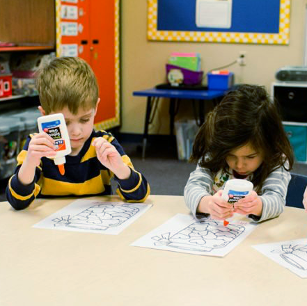 A boy and a girl are sitting at a table playing with glue