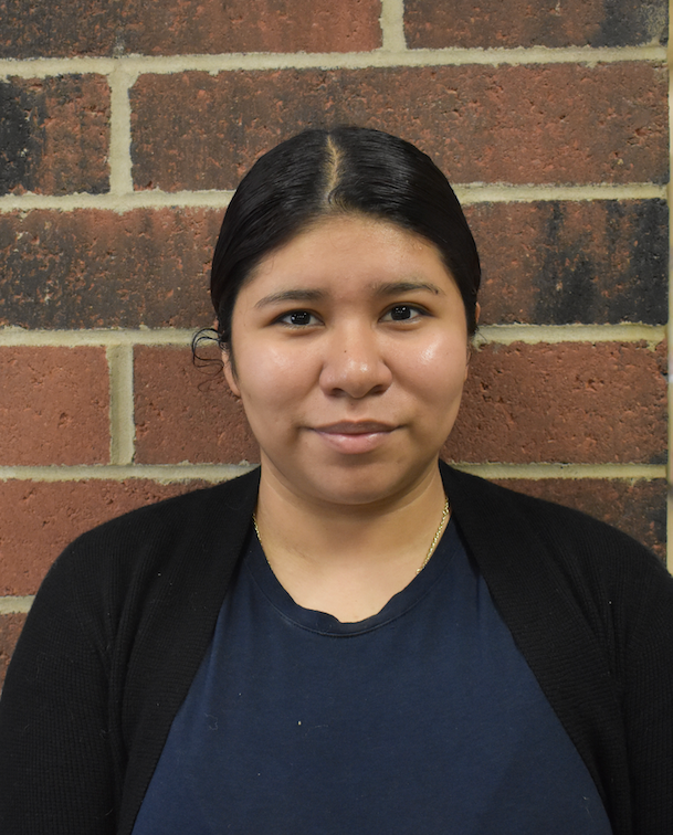 A woman with curly hair is wearing a blue tank top and smiling.