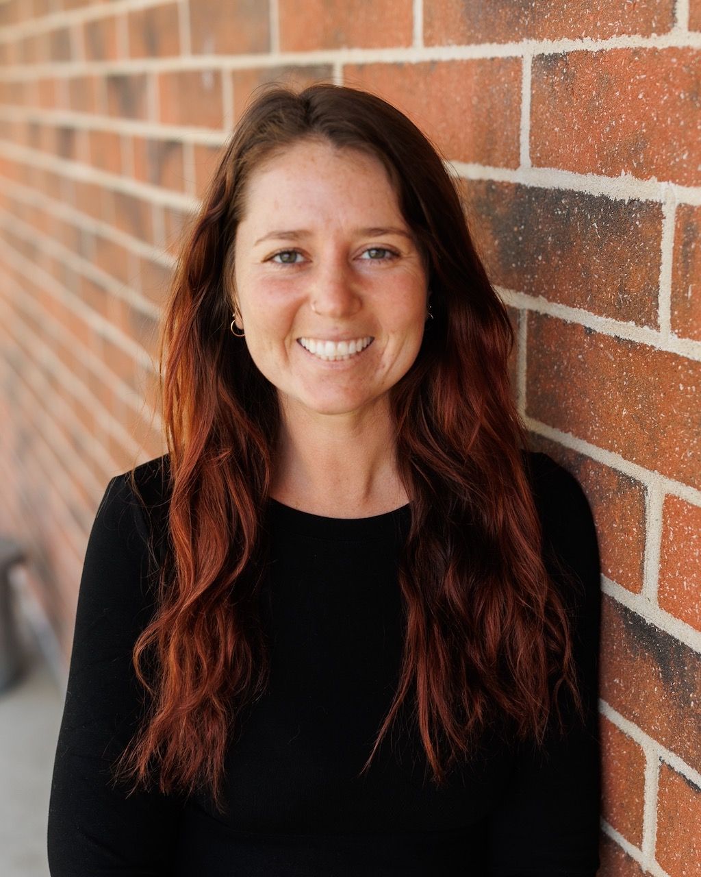 A woman with curly hair is wearing a denim shirt and smiling for the camera.