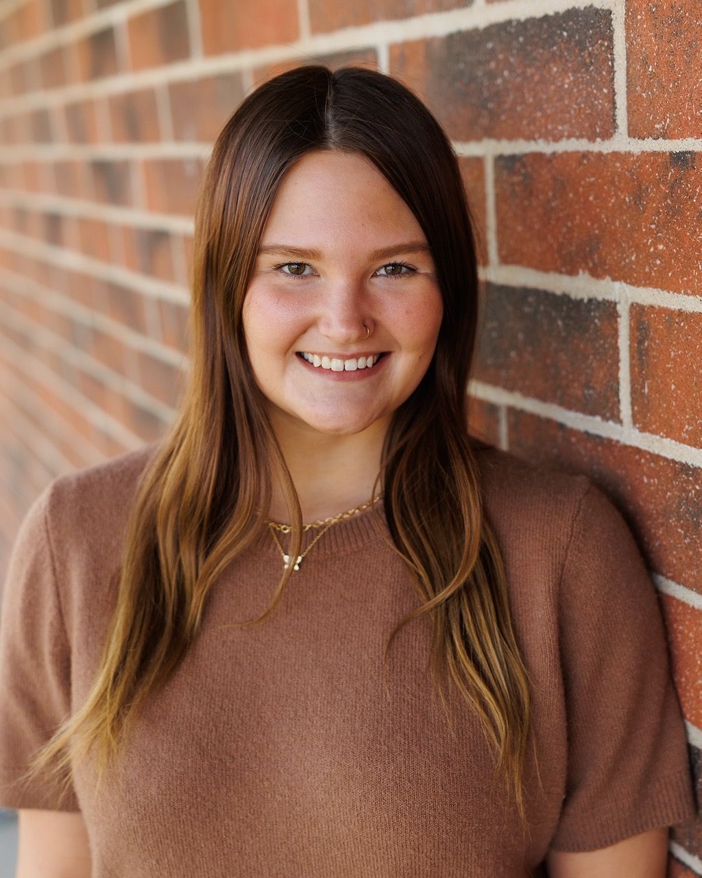 A woman with curly hair is wearing a denim shirt and smiling for the camera.