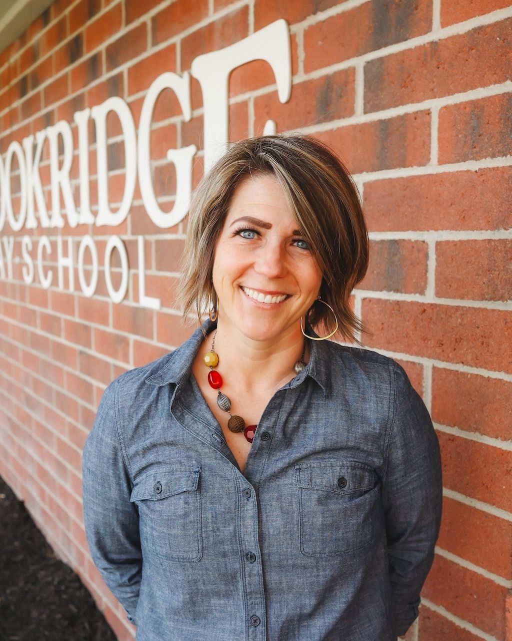 A woman in a green sweater and black lace collar is smiling for the camera.