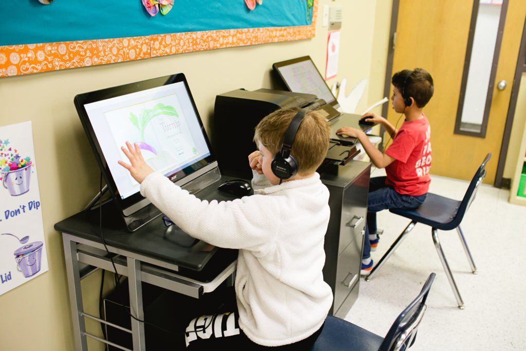 A boy wearing headphones is using a computer in a classroom.
