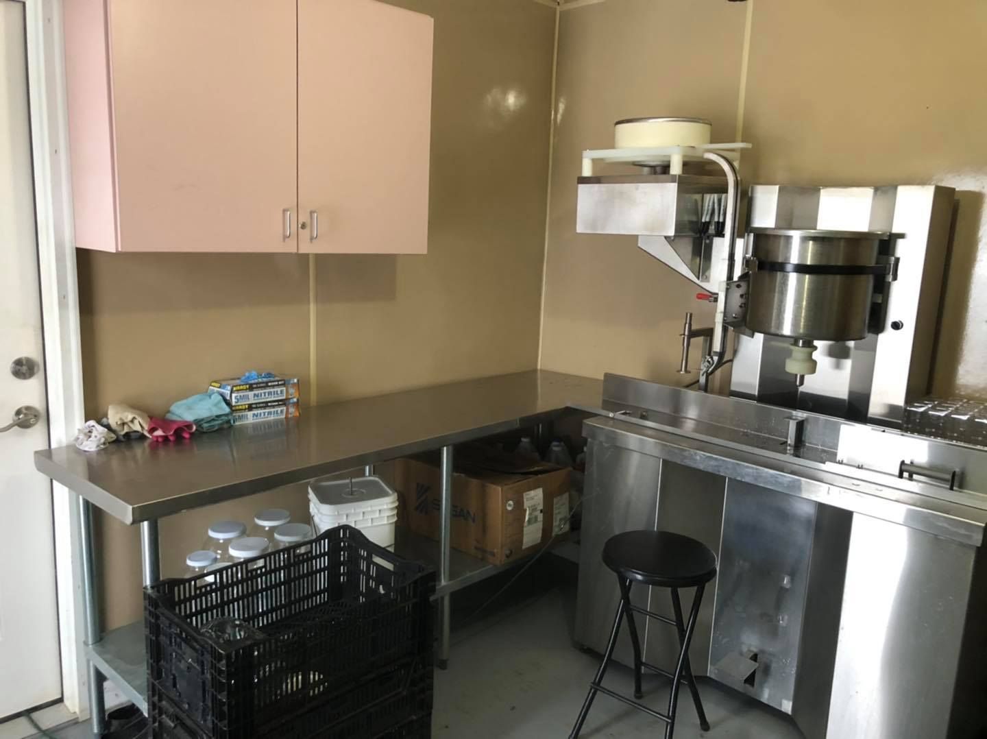 A light-tan kitchen corner with stainless steel countertops, a commercial dispenser, a black crate, and pink cabinets.