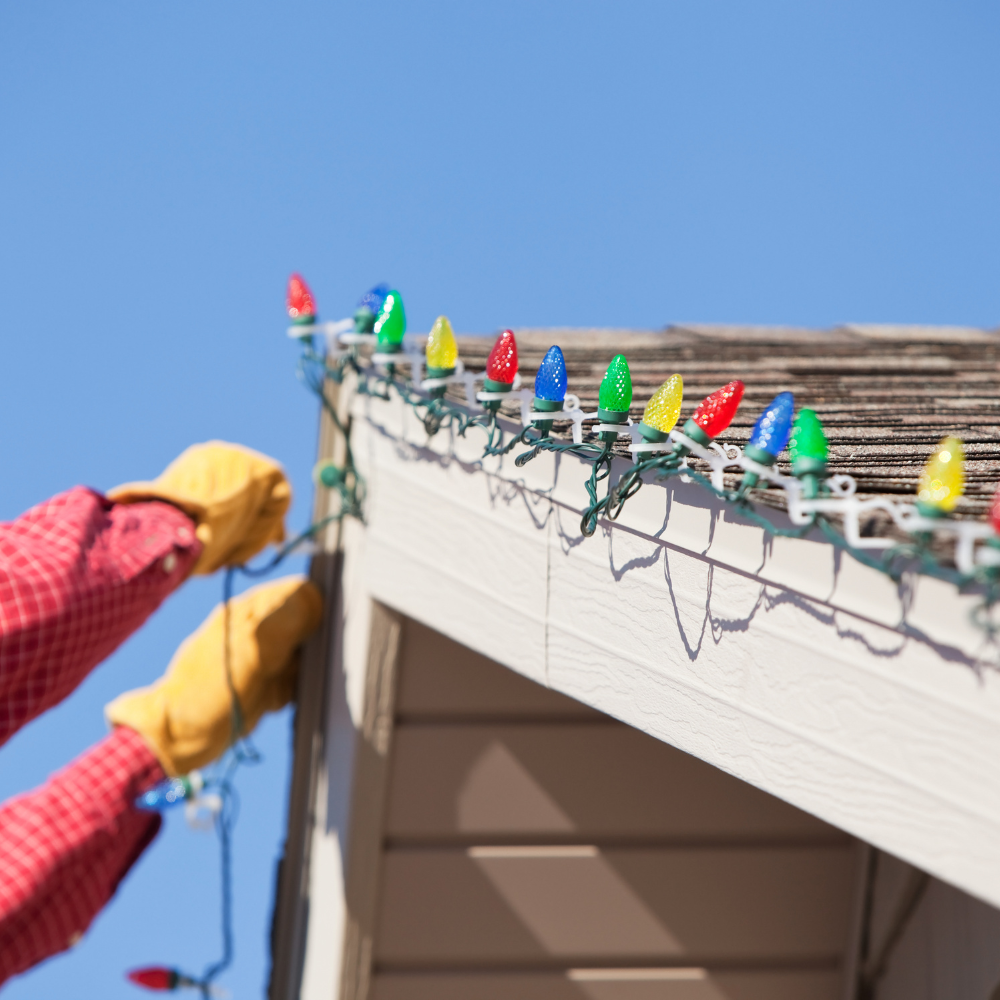 A person is hanging christmas lights on the side of a house
