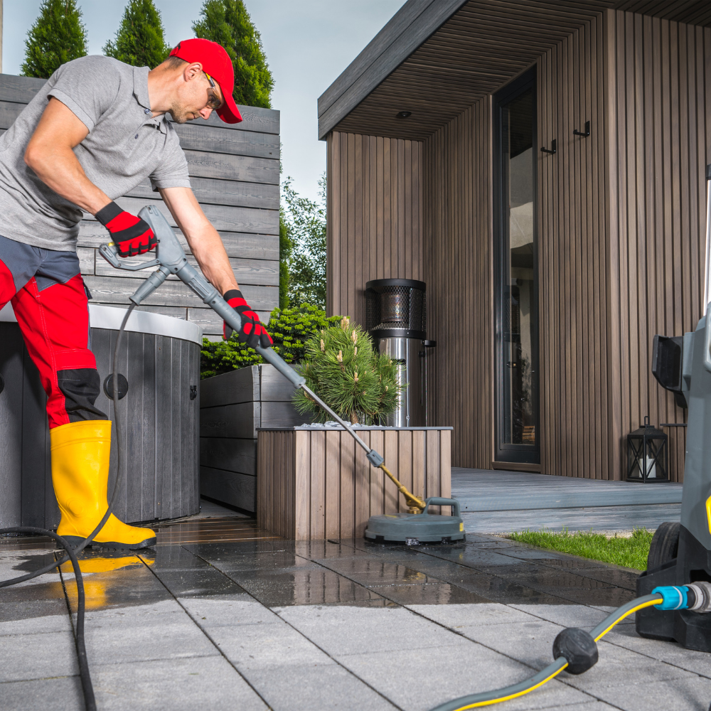 A man wearing yellow boots is cleaning a patio with a vacuum cleaner.