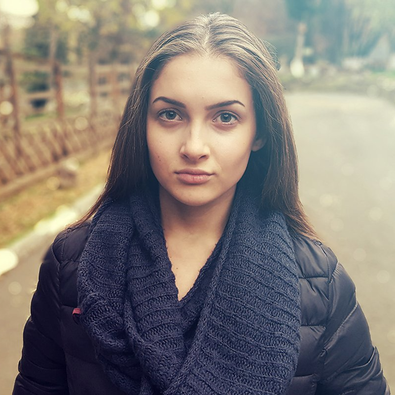 Woman with long brown hair wearing a dark blue scarf and jacket, looking straight at the camera.