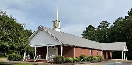 Brick church with white steeple and red front porch surrounded by trees