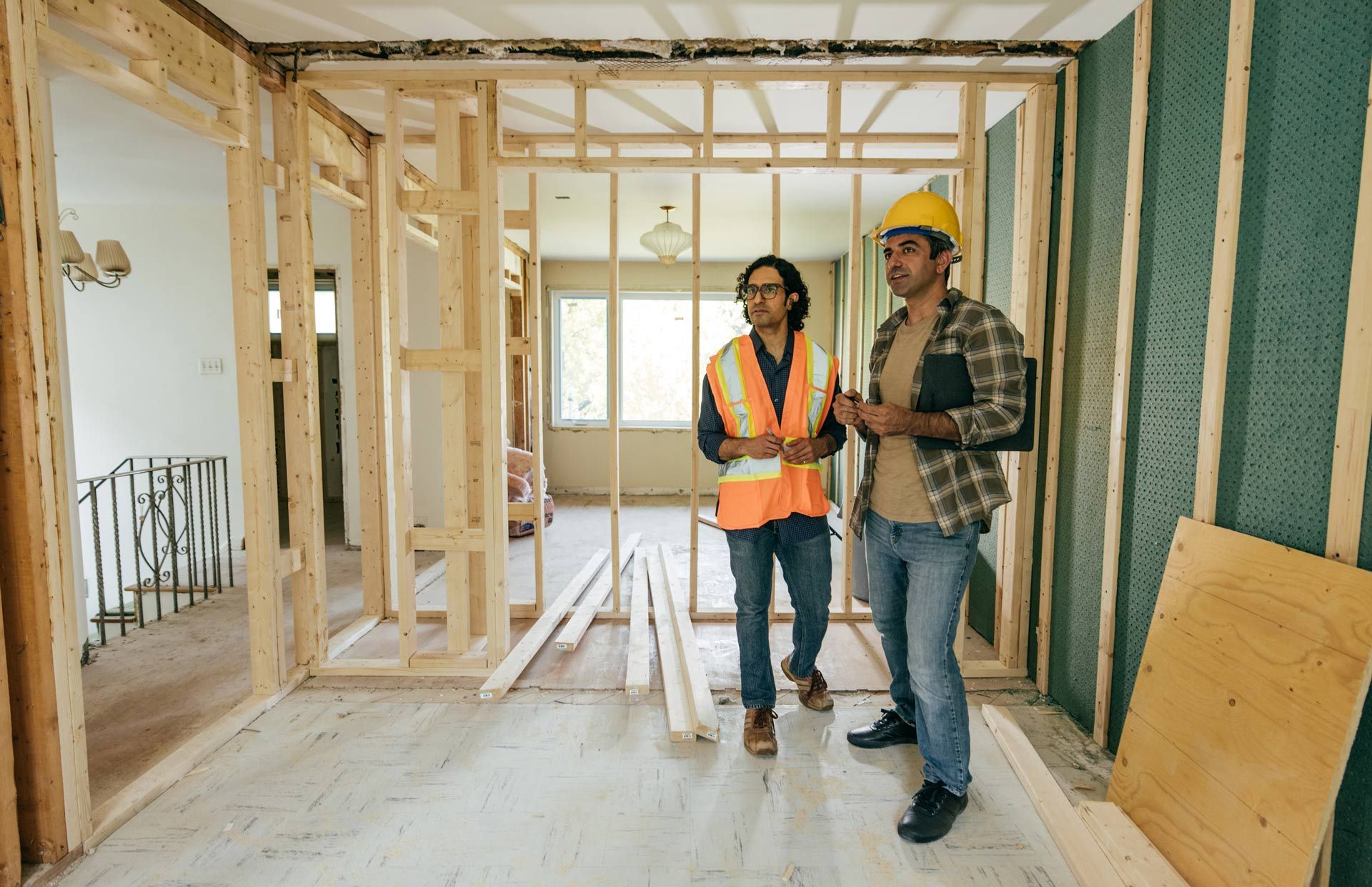Two construction workers are standing in a room under construction