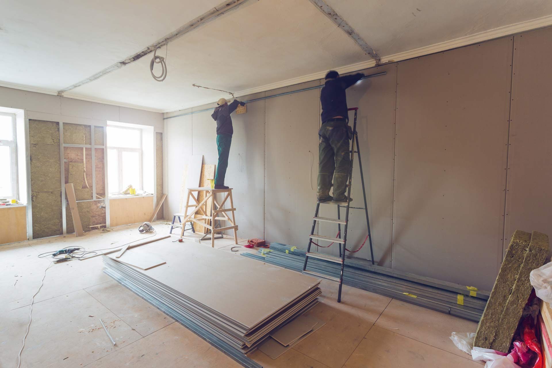 Two men are working on a wall in a room
