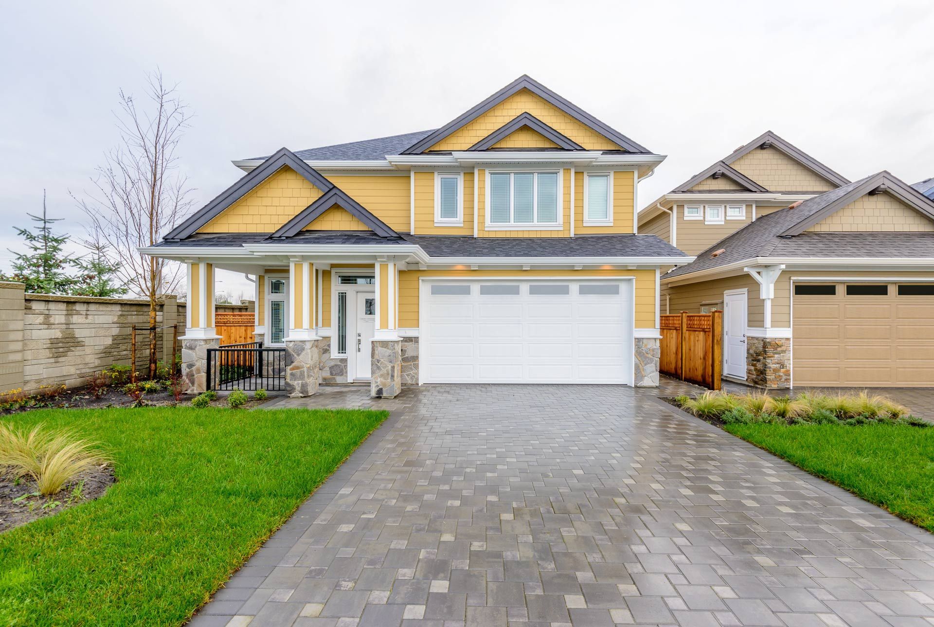 A large yellow house with a white garage door and a brick driveway