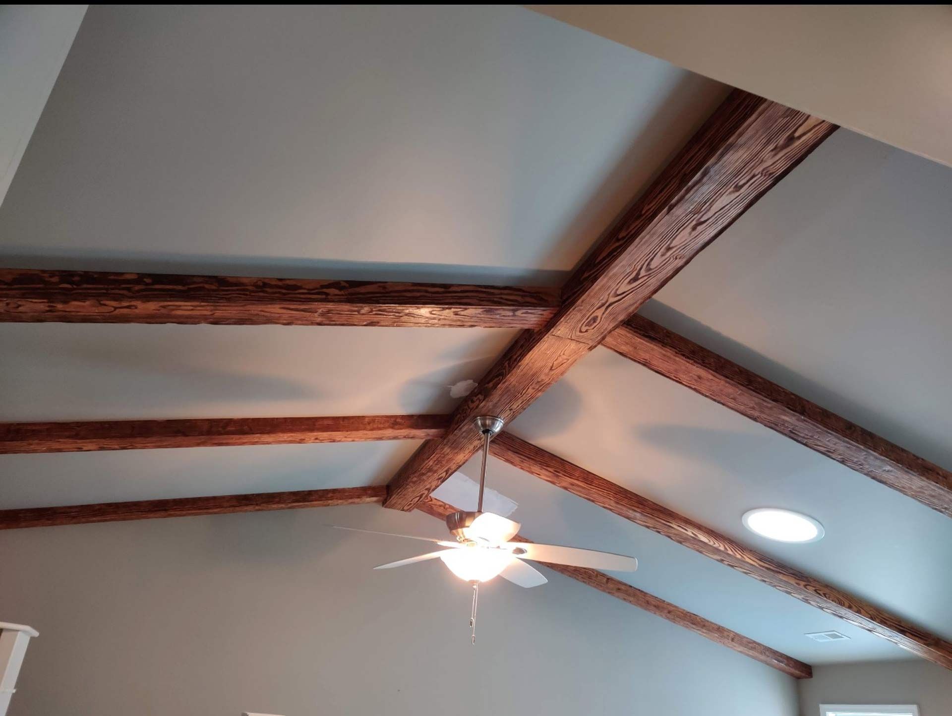 A vaulted ceiling with wooden beams and a ceiling fan