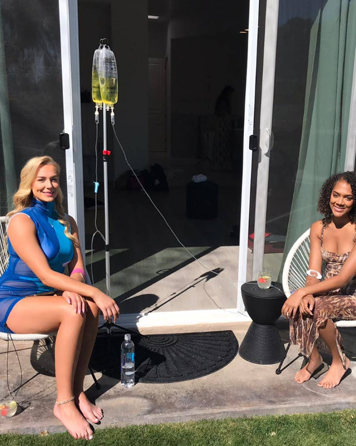 Two women outside receiving IV drips in sunny setting.