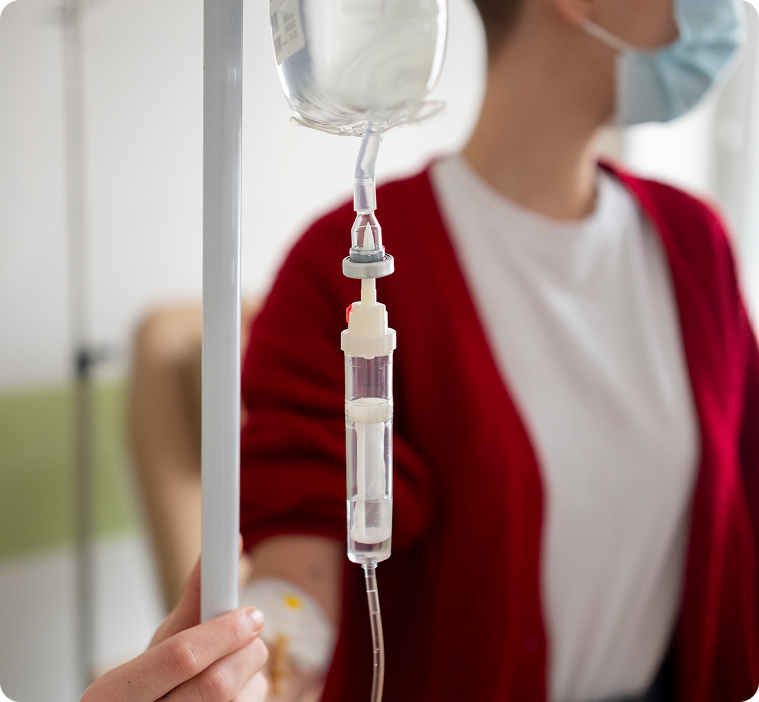 Person receiving IV fluids in a medical setting, nurse visible.