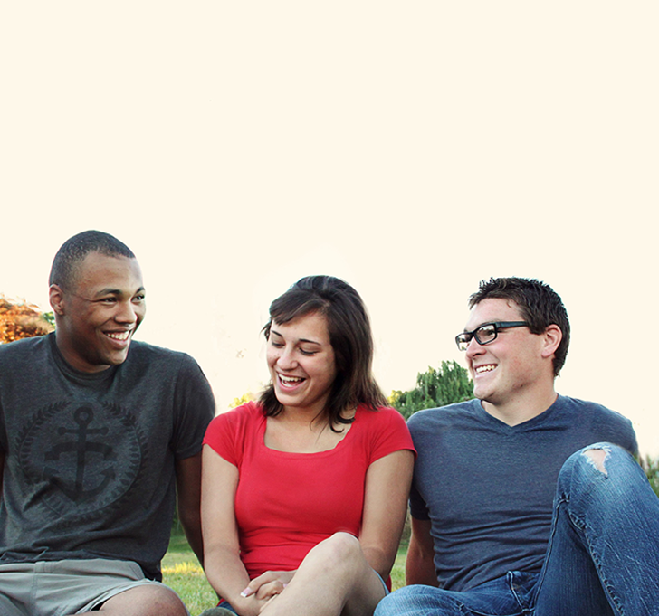 Three young adults sitting outside, laughing. Black man on left, woman in middle, white man on right.