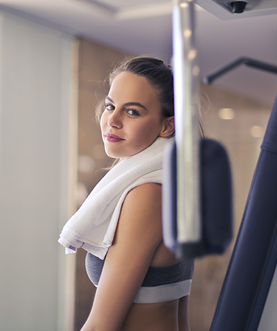 Woman in gym with towel around neck, looking at the camera.