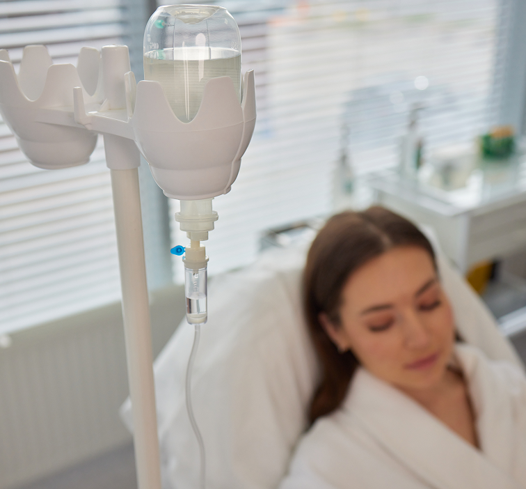 IV drip bag hanging above a woman lying in a bed, likely receiving medical treatment.