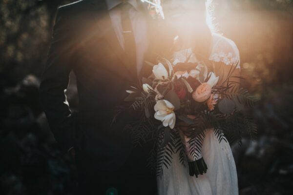 Bride and groom embrace in sunlight, bride holding bouquet of flowers.