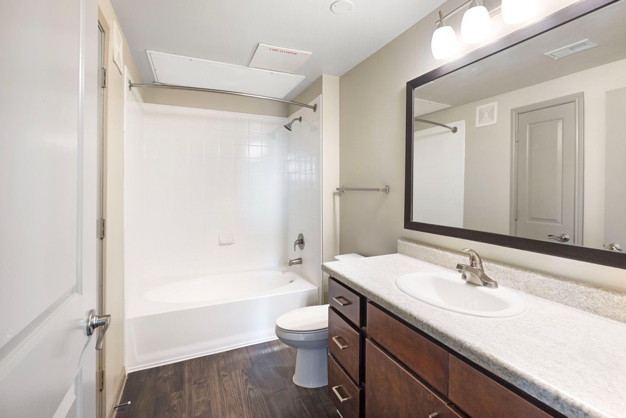 Apartment bathroom with vanity, sink, mirror, toilet, and shower/tub.