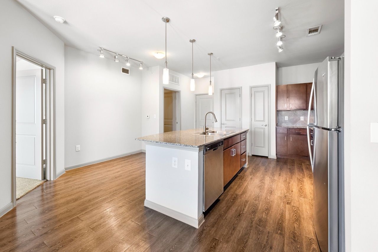 Open-concept kitchen with island, stainless fridge, pendant lights, and wood flooring.