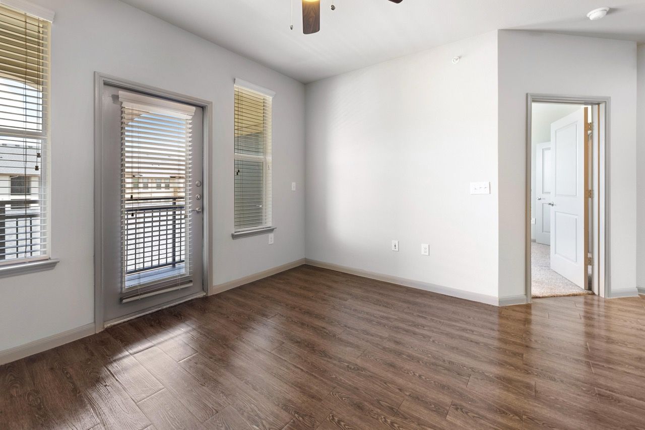 Empty living area with laminate flooring, two windows, and a door to a balcony.