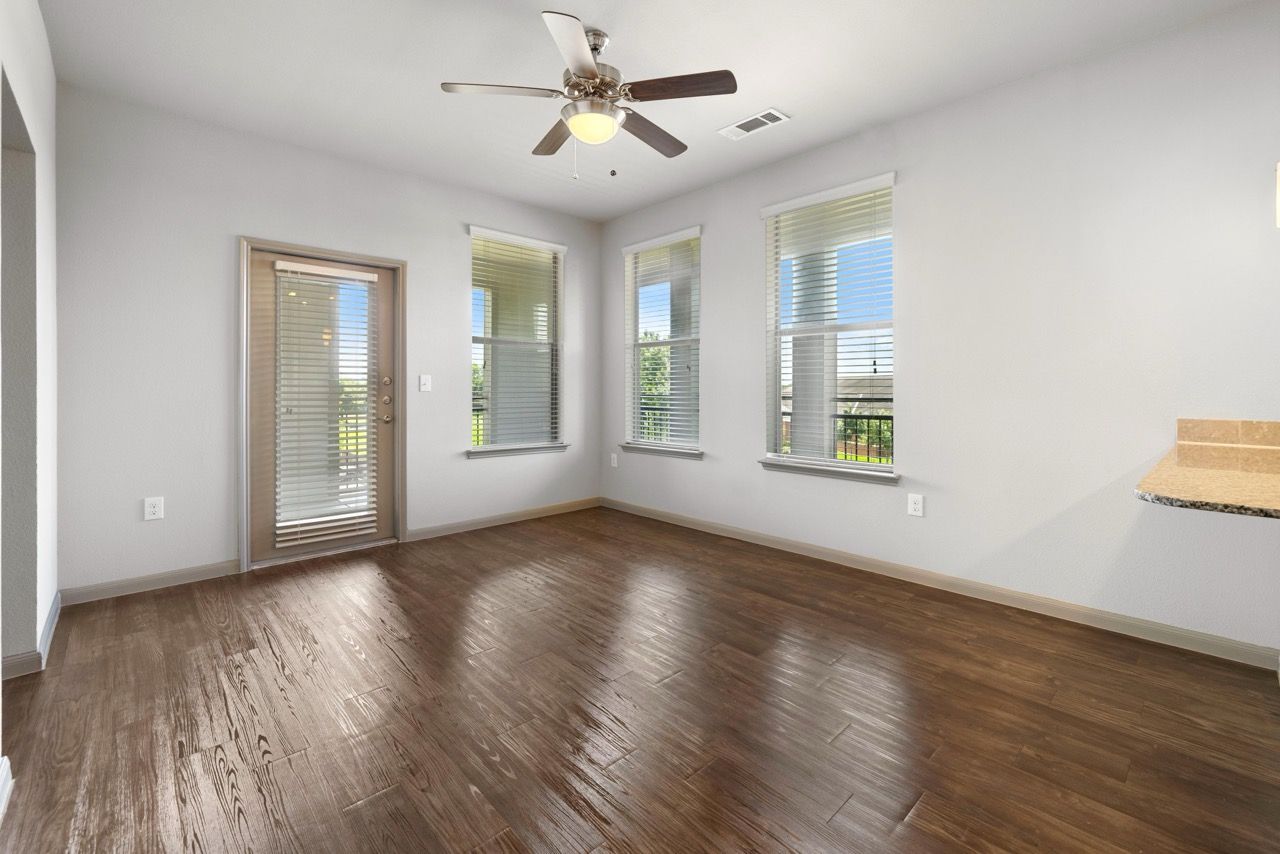 Living room with wood-look flooring, ceiling fan, and large windows with a balcony door.