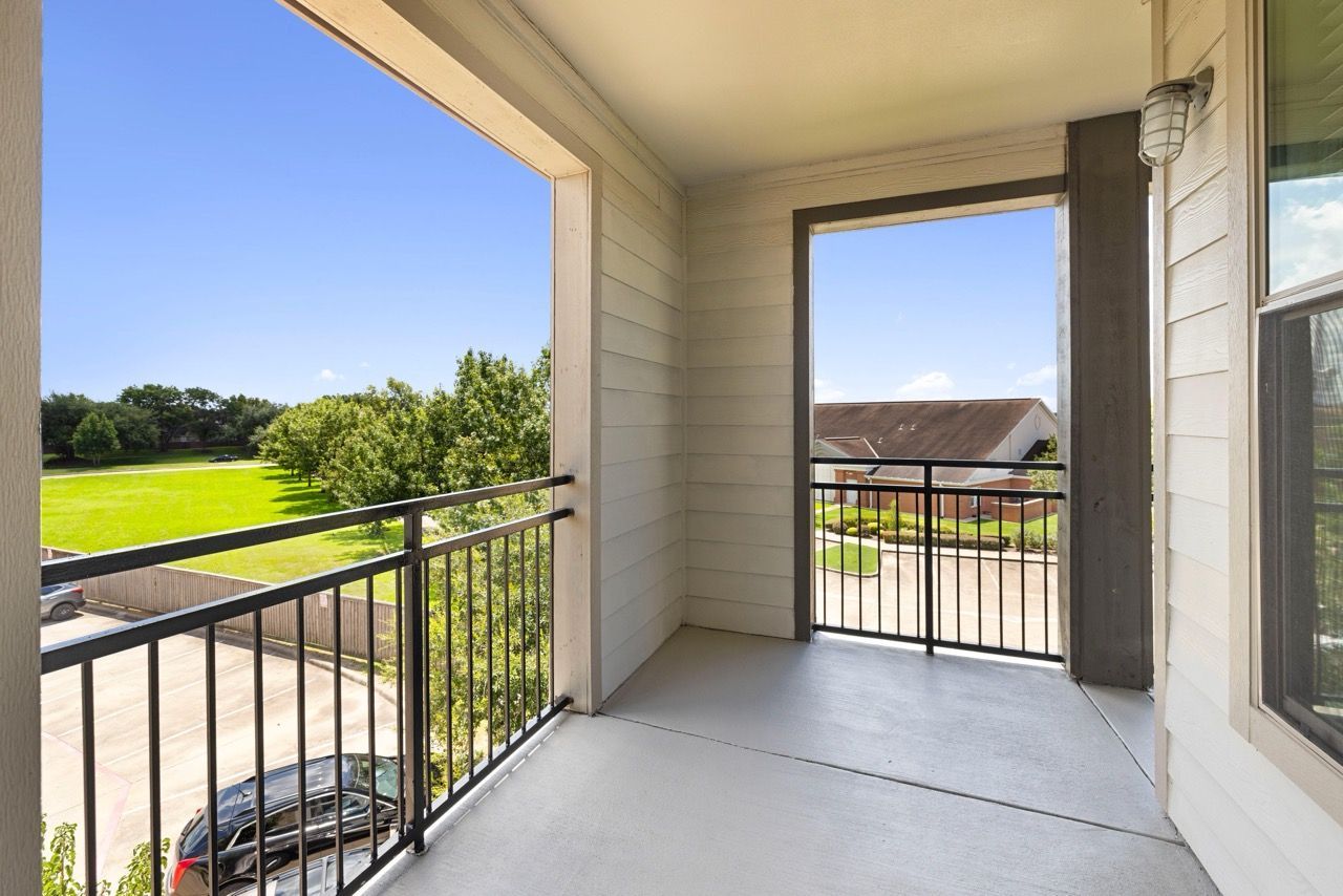 Balcony with black metal railing, view of green lawn, trees, and nearby buildings.