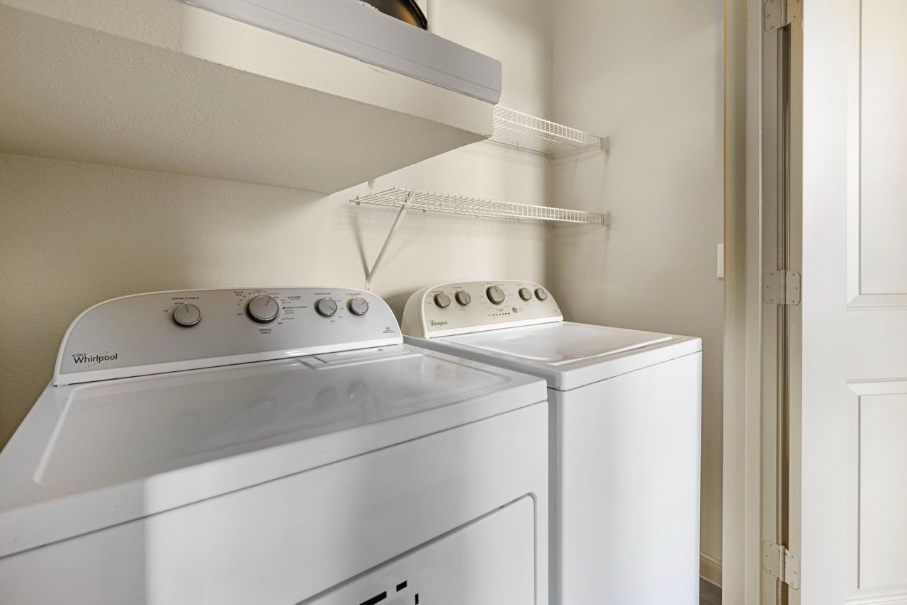 Laundry closet with white side-by-side washer and dryer and wire shelving.