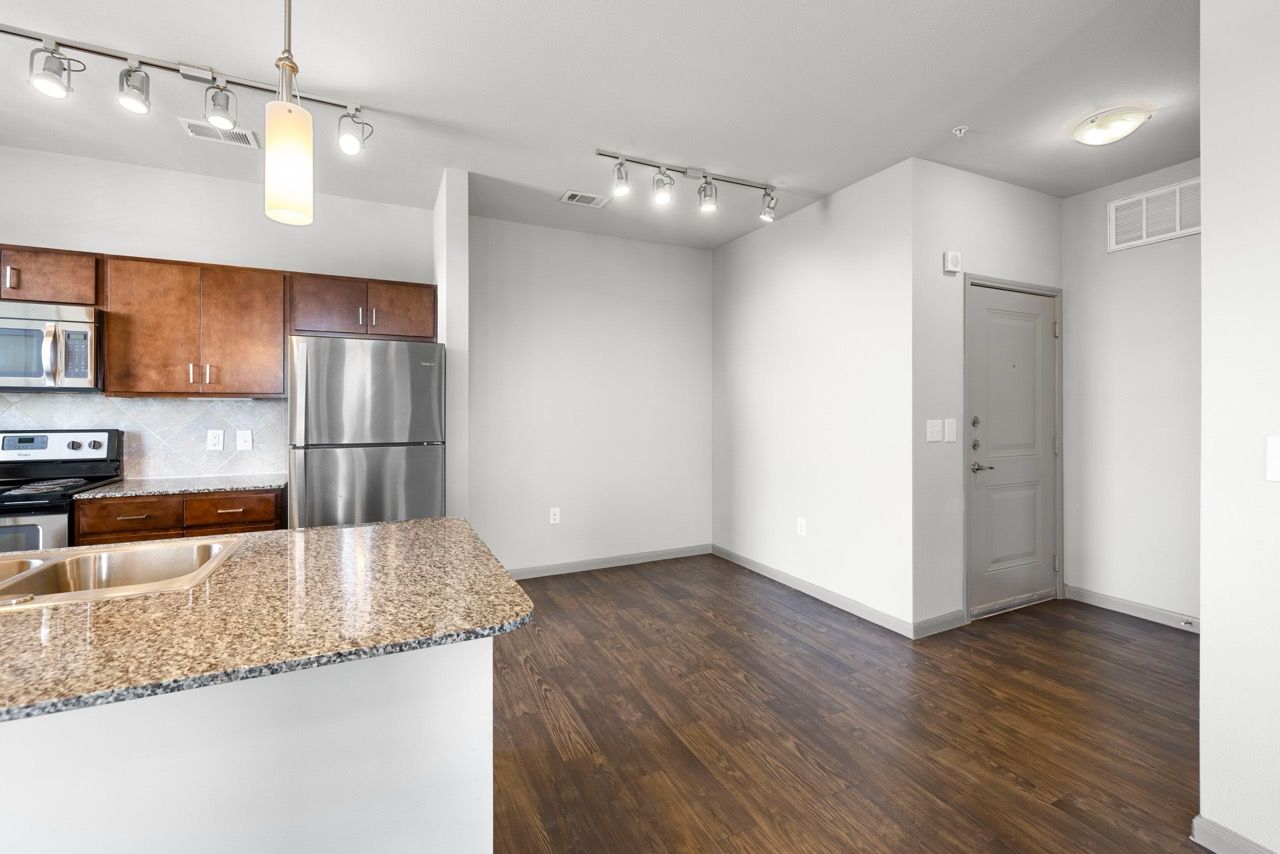 Open-plan apartment kitchen with granite counters, stainless-steel appliances, and dark wood flooring.