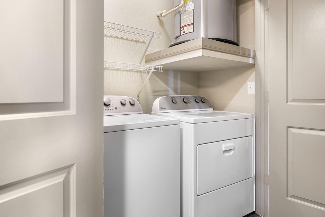 Laundry closet with a washer and dryer side by side and a water heater on a shelf above.