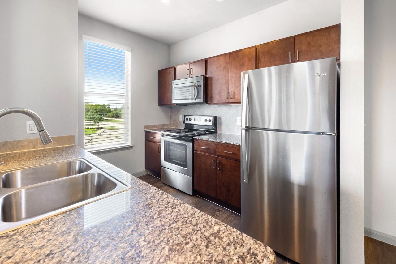 Bright apartment kitchen with a double sink, granite countertops, and stainless steel appliances.