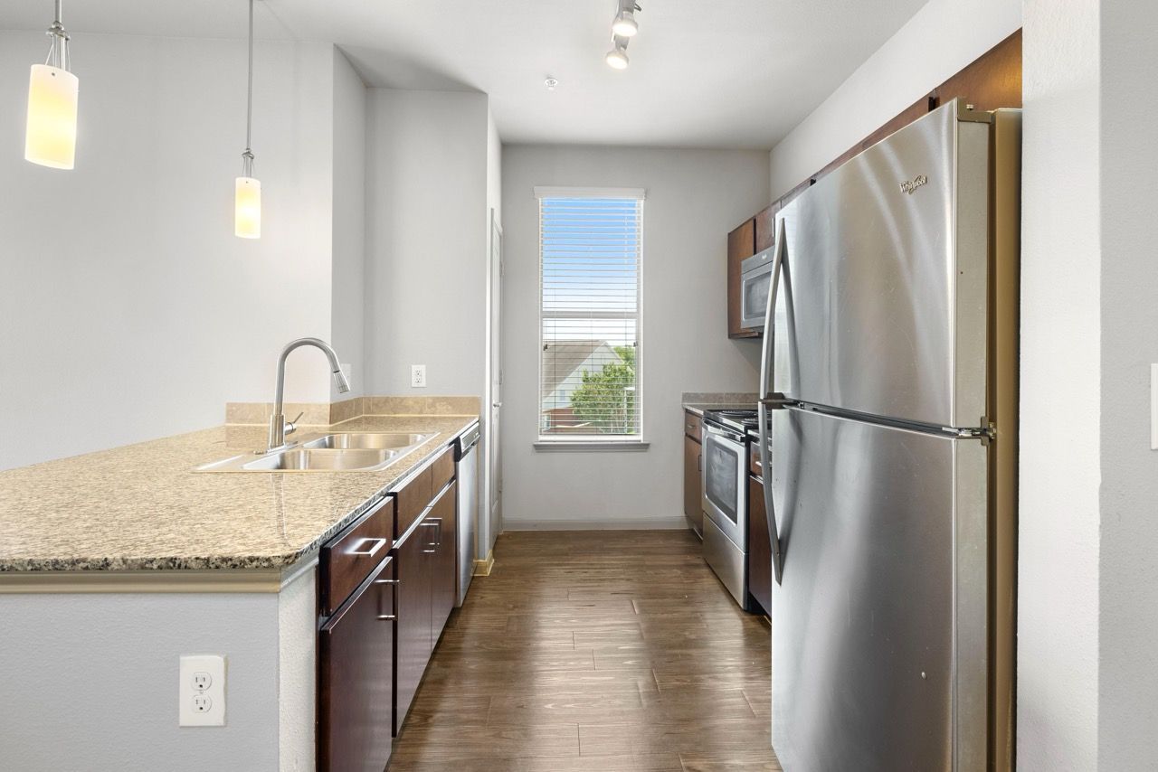 Modern kitchen with granite counters, stainless steel appliances, and a window at the far end.