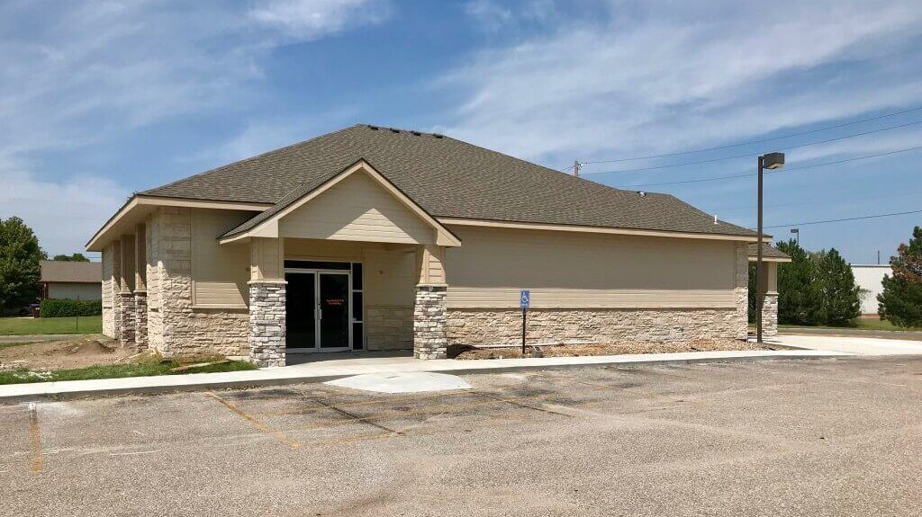 A small building with a stone facade is sitting on top of a gravel lot.