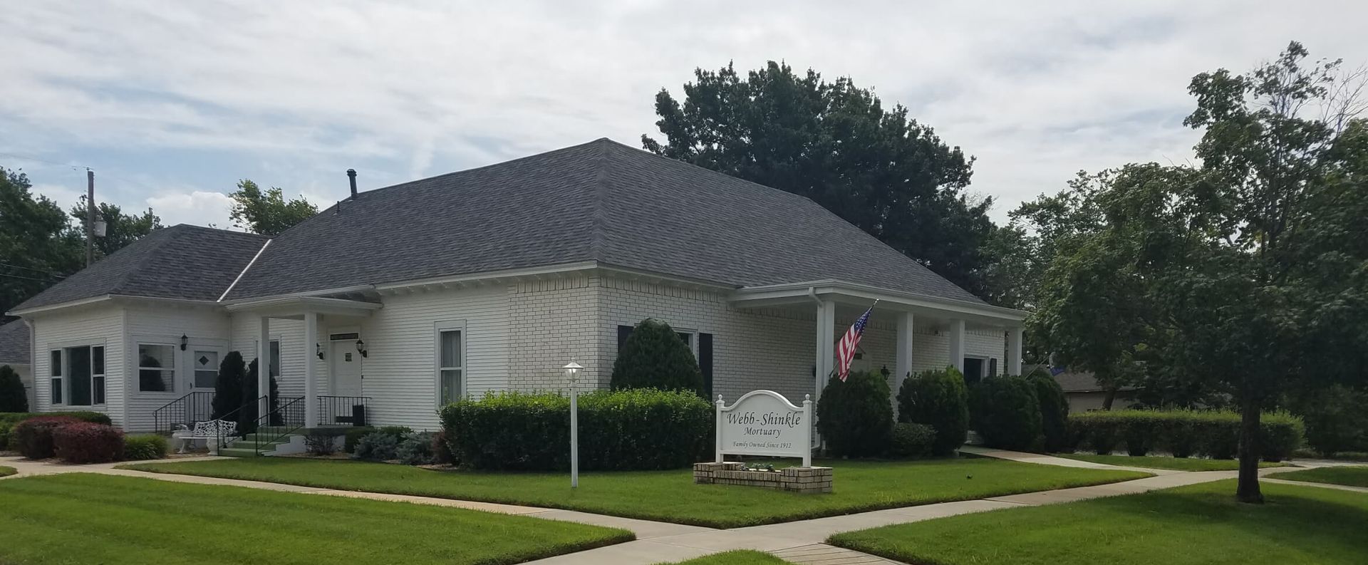 A white house with a black roof and a sign in front of it