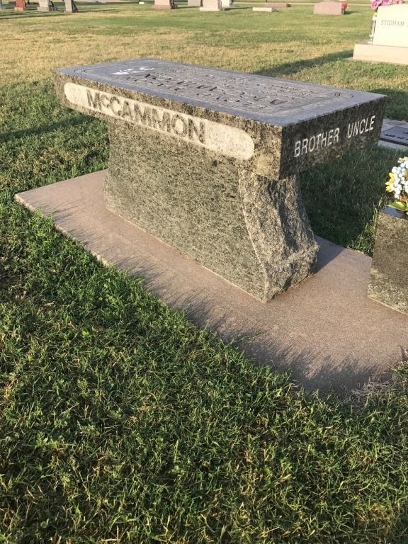 A grave with a bench in the grass in a cemetery.