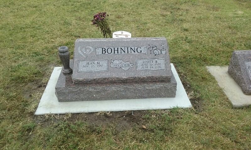 A grave in a cemetery with a vase and a flower on it.
