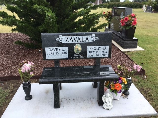 A grave with a black bench and flowers in front of it.