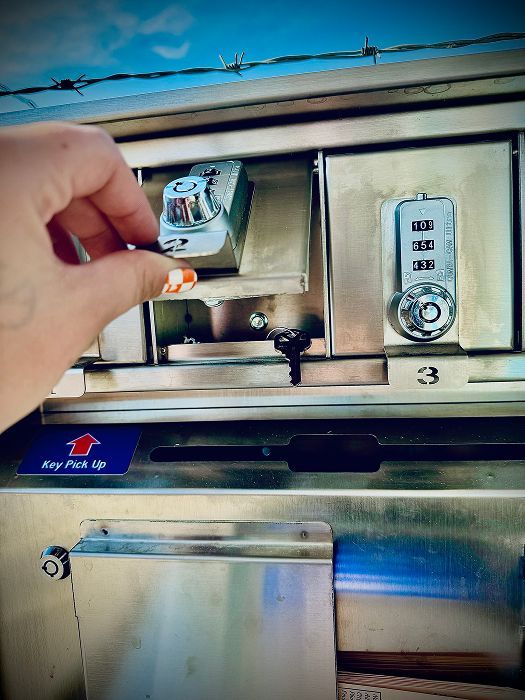 Hand placing a key in a metal key box with a combination lock, likely for mail pickup, outdoors. | King's Auto LLC