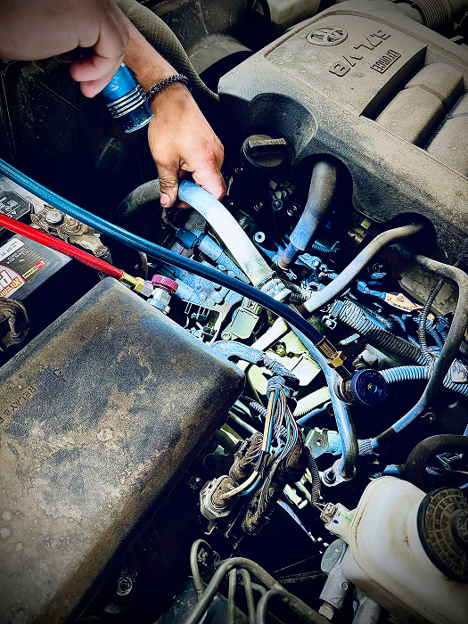 Mechanic working on a car engine. Hands are near hoses with gauges in an engine bay. | King's Auto LLC