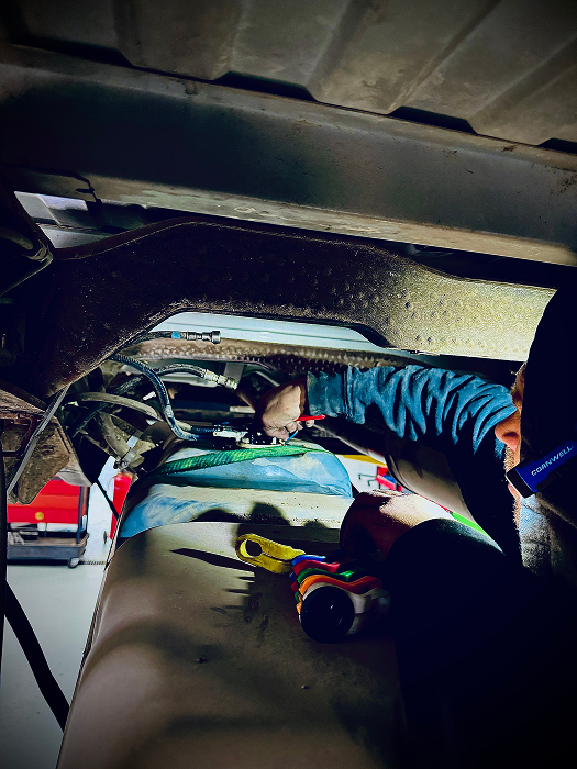 Person working under a vehicle, using tools and a flashlight, dropping a fuel tank | King's Auto LLC