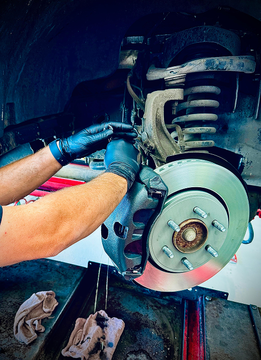 Mechanic in black gloves working on a car's brake rotor in a garage setting. | King's Auto LLC