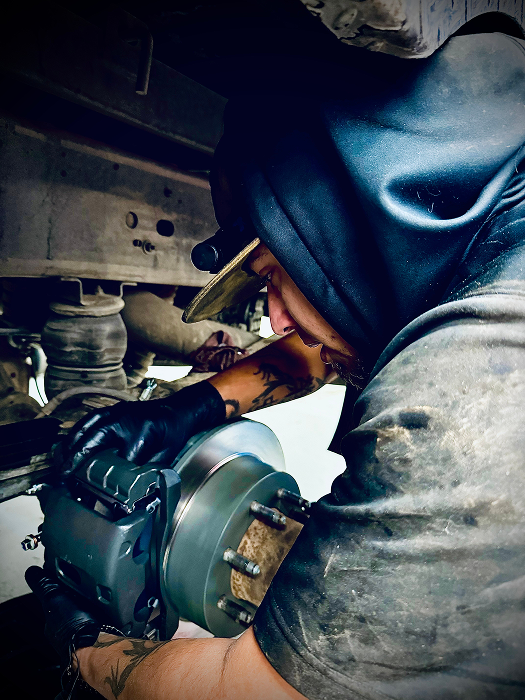 A person works on a vehicle's brake. Black gloves and a dirty shirt. | King's Auto LLC