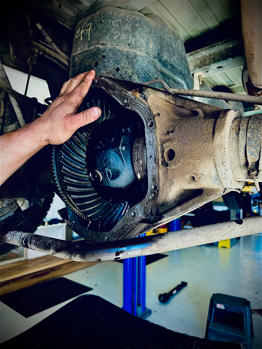 Open differential on a vehicle with hand, gear teeth visible. Workshop setting, blue lift. | King's Auto LLC