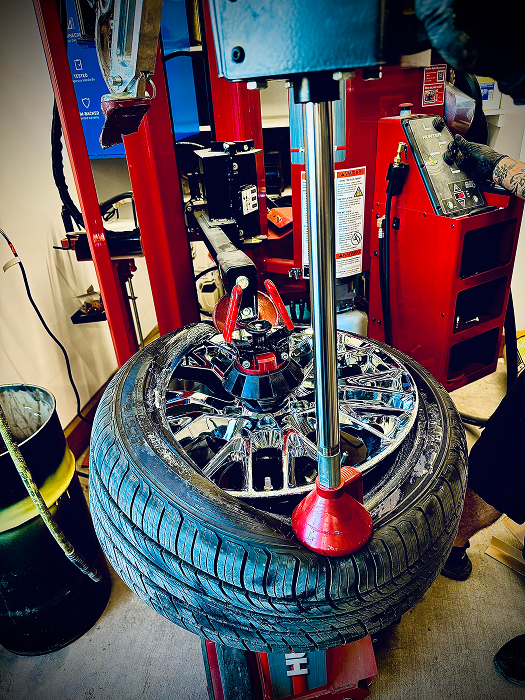 Tire being removed from a chrome rim by a red tire machine in a garage. | King's Auto LLC