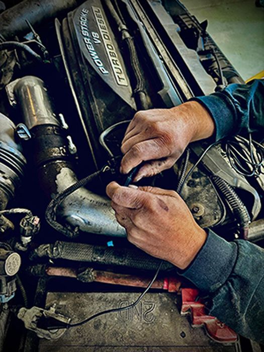 Mechanic's hands working on a diesel engine. Black wires, close-up shot. | King's Auto LLC