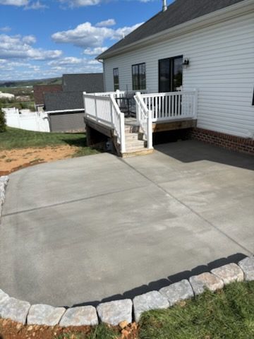 Newly poured concrete patio next to a white house with a deck. The patio has a stone border.